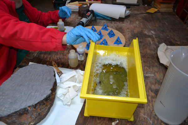 Person wearing gloves working with chemicals in a yellow container.
